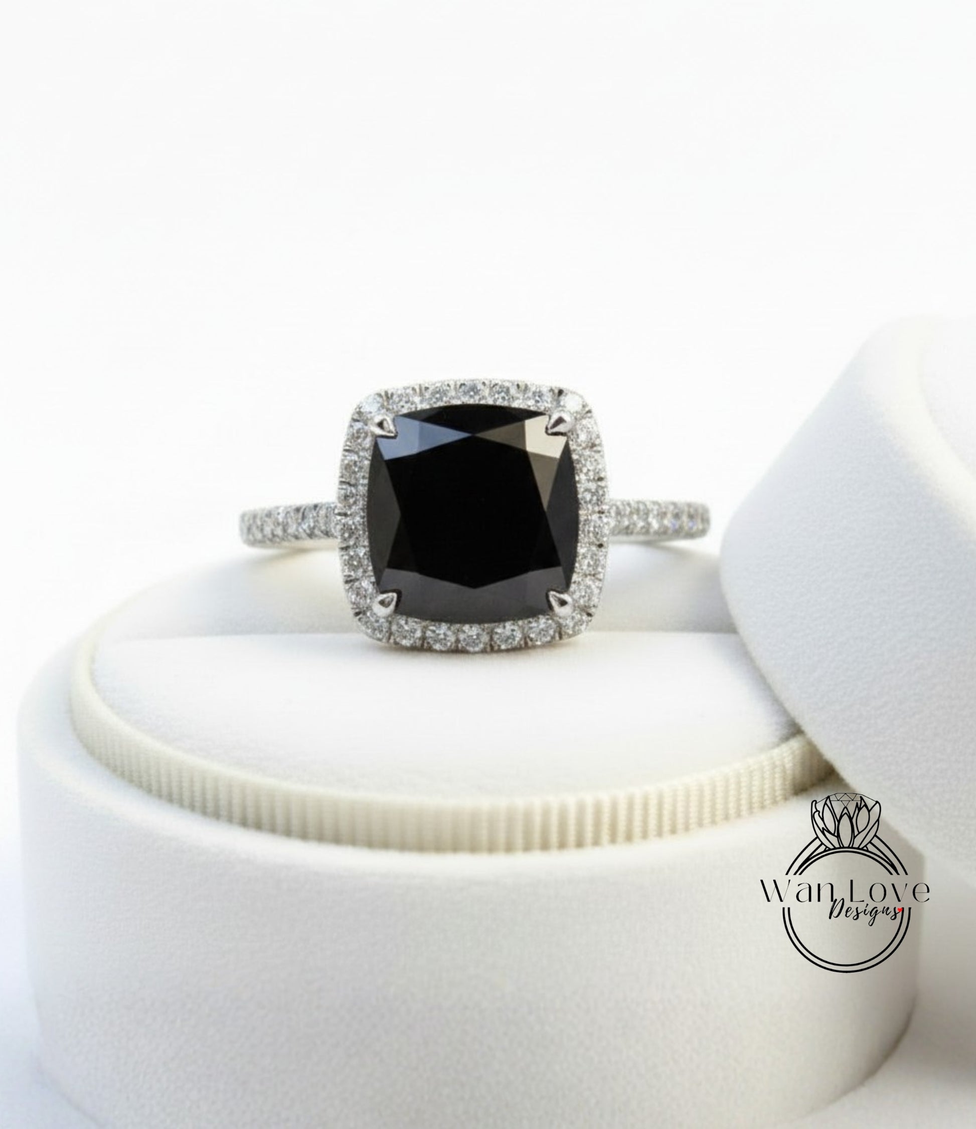 A diamond engagement ring with a large black gemstone set in a halo of smaller diamonds, displayed on a white stand.