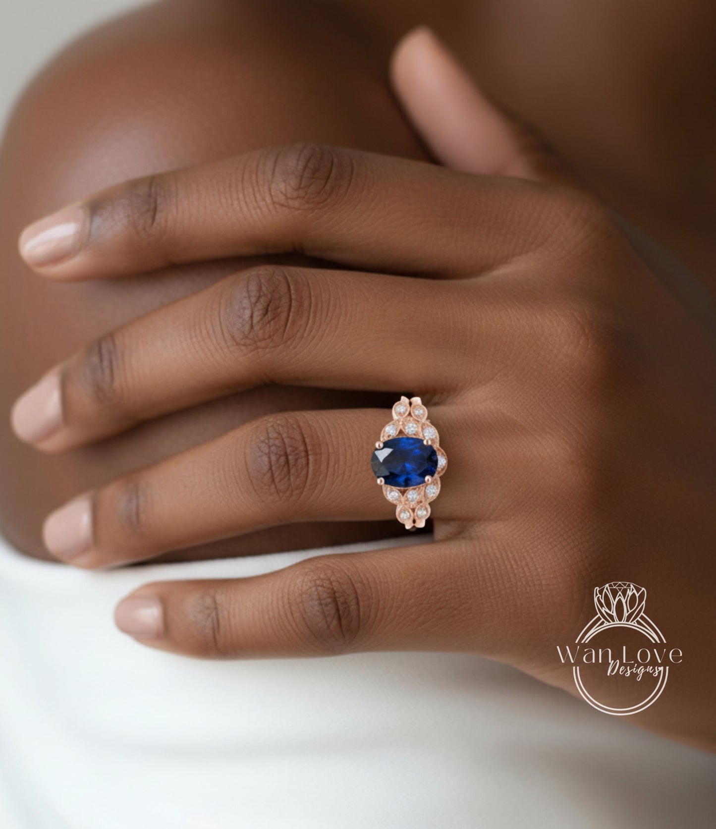 A close-up of a hand wearing a ring with a large blue gemstone, resting on a white surface.