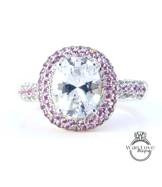A large, oval-shaped diamond ring with a halo of smaller diamonds around the center stone, set in a silver band with purple gemstones.