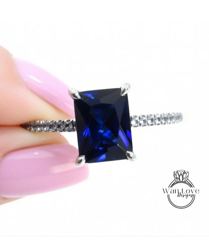 A close-up of a person's hand holding a ring with a large blue gemstone, likely a sapphire, on a silver band.