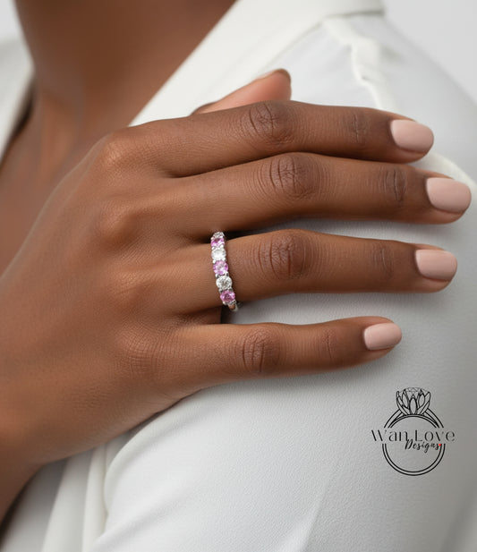 A close-up of a person's hand wearing a ring with a row of pink gemstones.