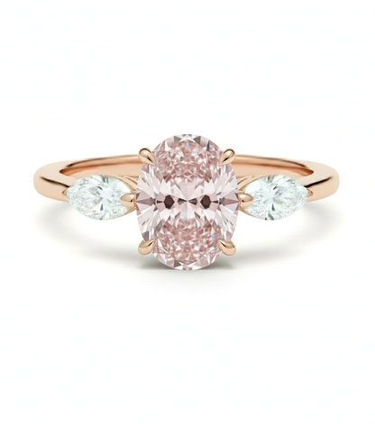 A rose gold engagement ring with a large oval-shaped pink diamond set in the center, flanked by two smaller diamonds on either side.