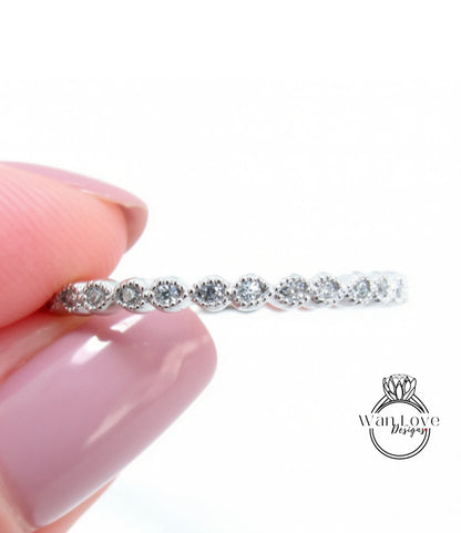 A close-up image of a person's hand holding a delicate ring with a row of small diamonds on the band.