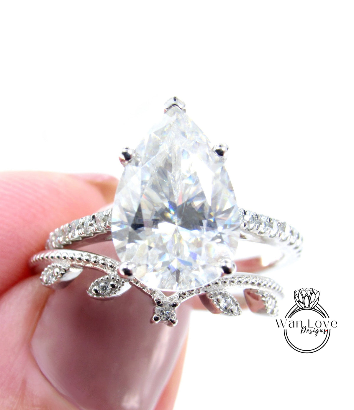 A close-up image of a person's hand holding a diamond engagement ring with a large pear-shaped diamond set in a ring band.
