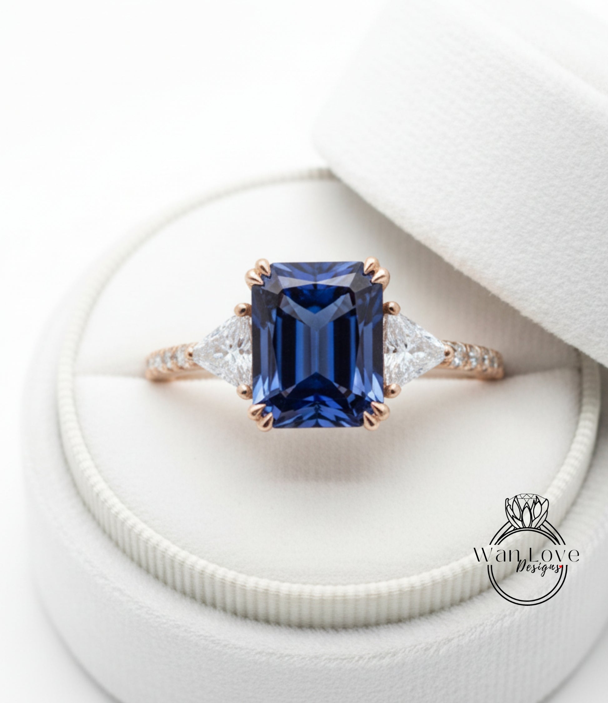 A close-up view of a diamond engagement ring with a large blue gemstone set in a gold band, placed in a white jewelry box.