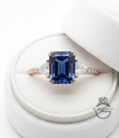 A close-up view of a diamond engagement ring with a large blue gemstone set in a gold band, placed in a white jewelry box.