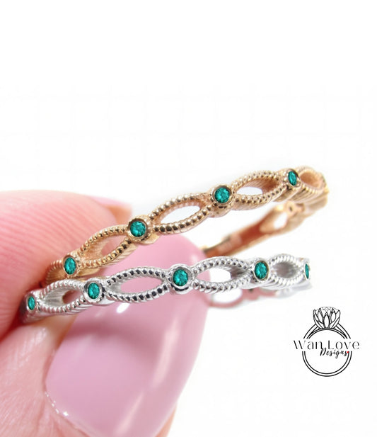 A close-up of a person's hand holding a ring with a decorative band and green gemstones.