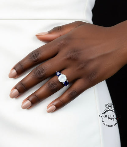 A close-up of a hand wearing a ring with a large white gemstone and blue gemstones.