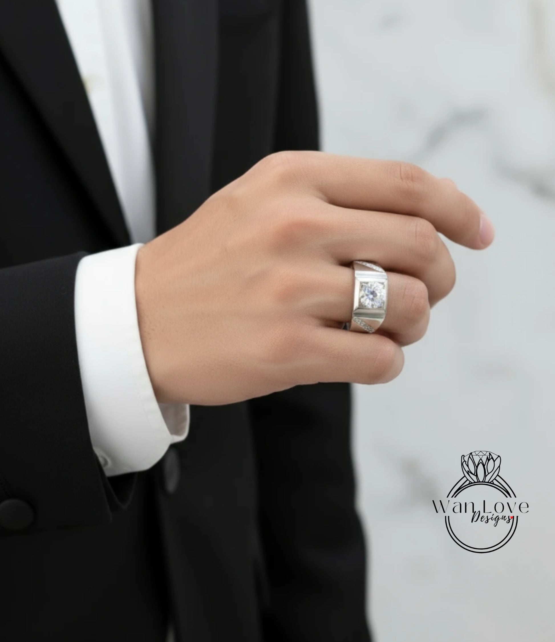 A close-up of a person's hand wearing a silver ring, with a black suit jacket visible in the background.