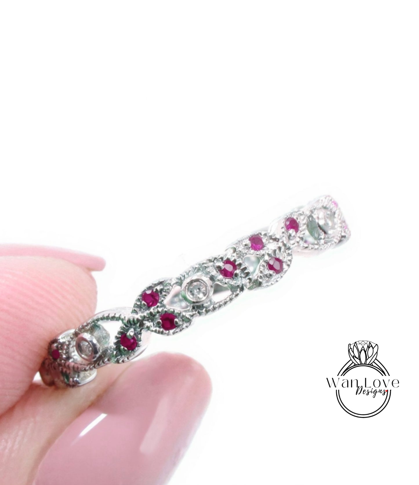 A close-up image of a person's hand holding a silver ring adorned with red gemstones.