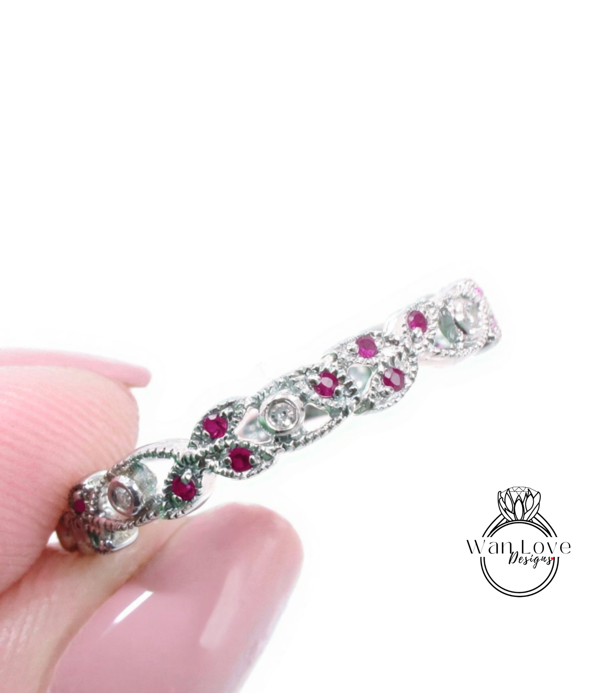 A close-up image of a person's hand holding a silver ring adorned with red gemstones.