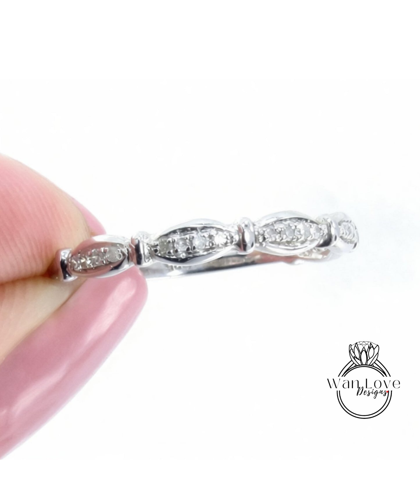 A close-up image of a person's hand holding a silver ring with a row of small diamonds on the band.