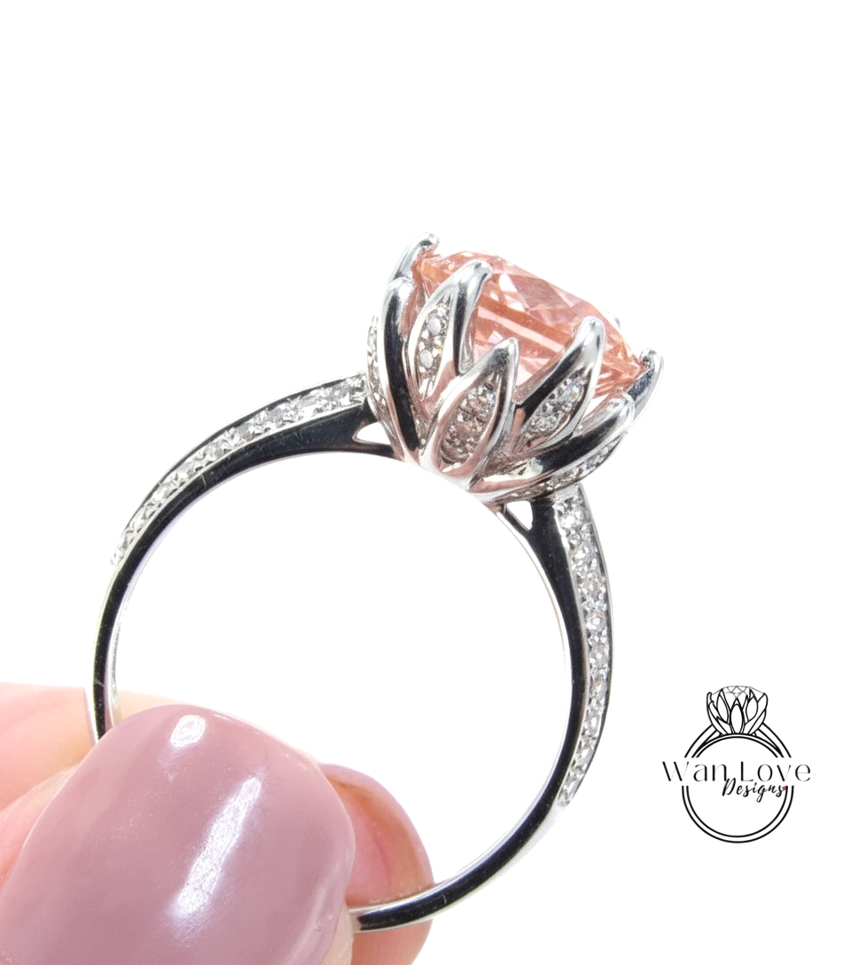 A close-up of a person's hand holding a silver ring with a large, pink gemstone.