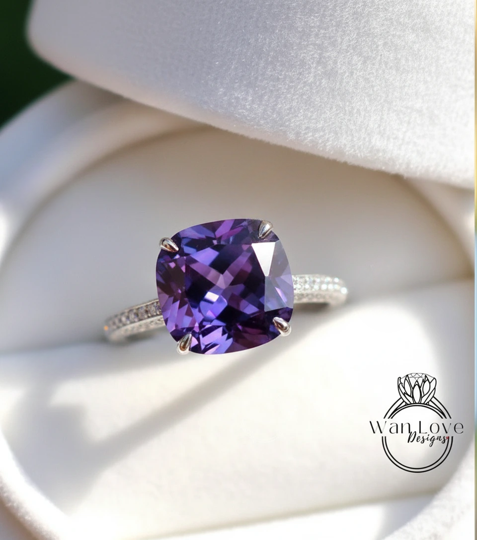 A close-up image of a silver ring with a large, deep purple gemstone, placed on a white background.