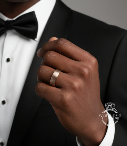 A close-up of a man's hand wearing a gold wedding band, with a black tuxedo jacket visible.