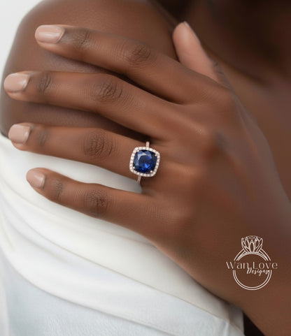 A close-up of a person's hand wearing a ring with a large blue gemstone, resting on a white fabric.
