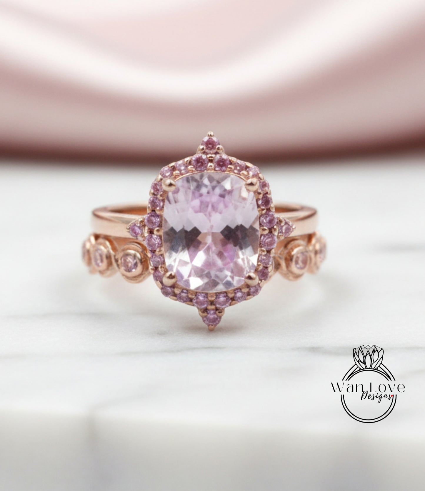 A close-up image of a pink gemstone ring with a large central gemstone surrounded by smaller gemstones and a halo of smaller gemstones around the central gemstone.