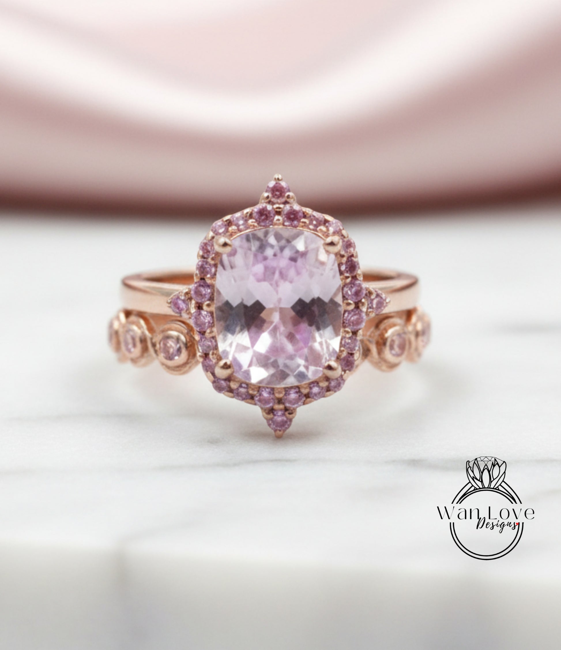 A close-up image of a pink gemstone ring with a large central gemstone surrounded by smaller gemstones and a halo of smaller gemstones around the central gemstone.