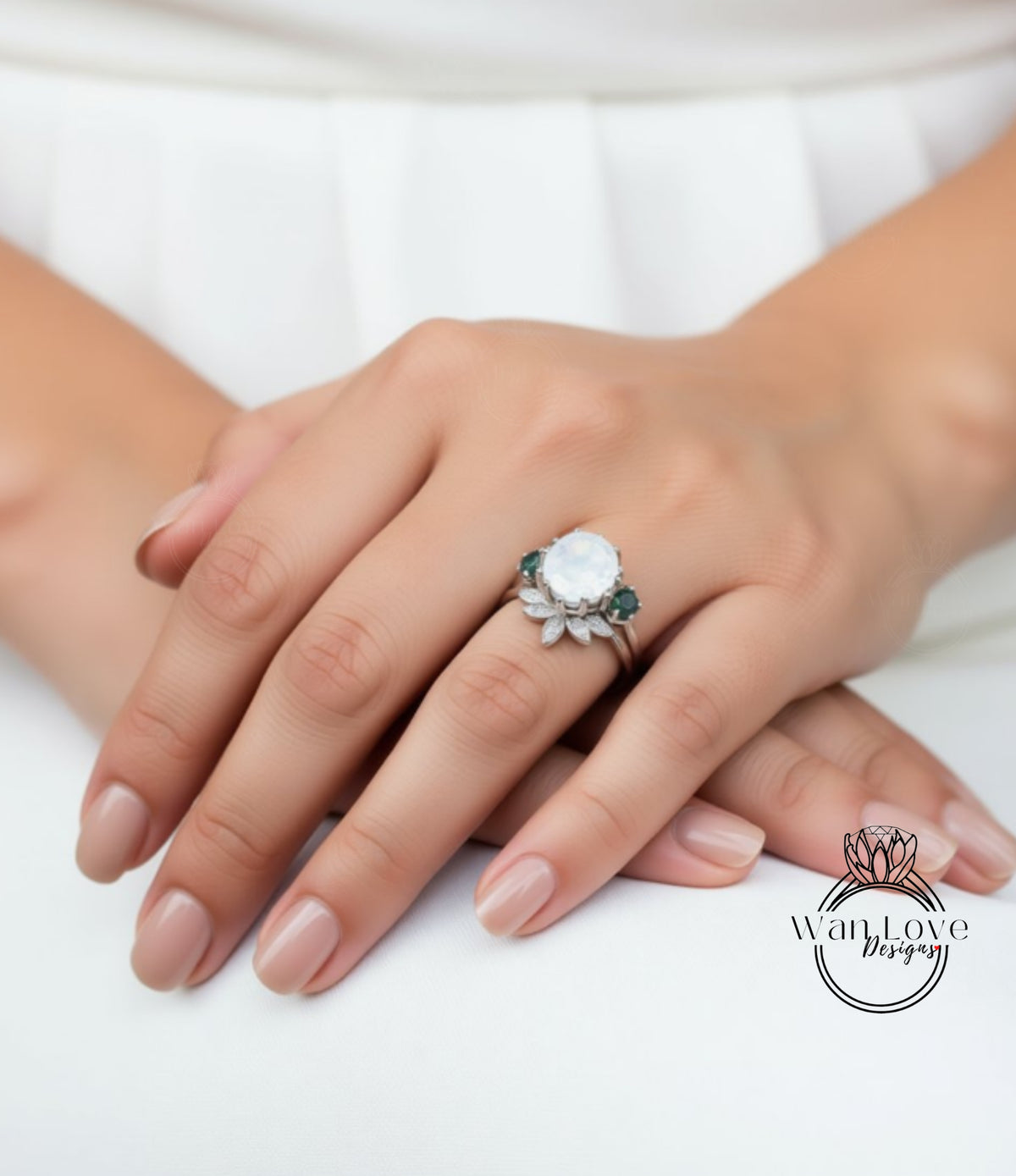 A close-up image of a person's hands wearing a ring with a large white gemstone and a floral design.