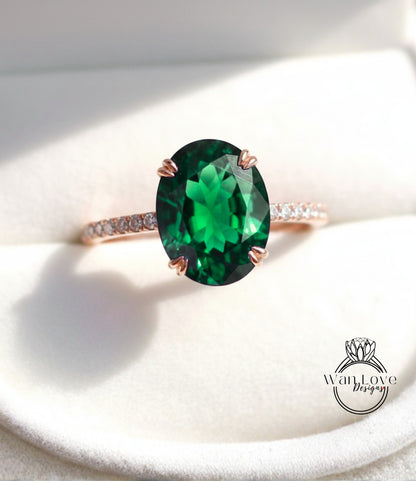A close-up image of a rose gold ring with a large oval-shaped green gemstone, such as a diamond, set in the center of the band.