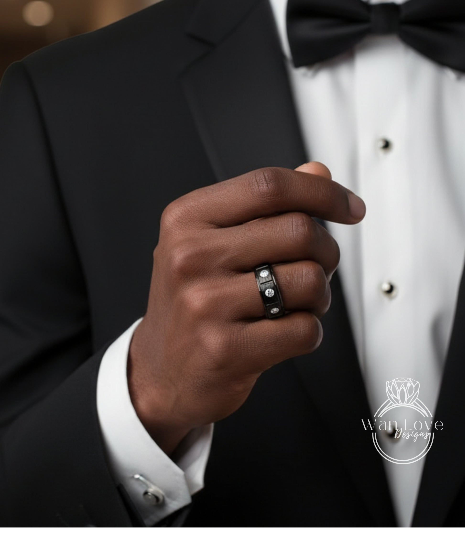 A close-up of a person's hand wearing a black ring with a diamond, wearing a black tuxedo jacket and bow tie.