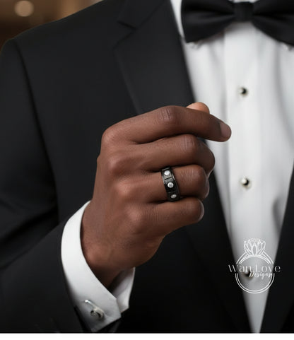 A close-up of a person's hand wearing a black ring with a diamond, wearing a black tuxedo jacket and bow tie.