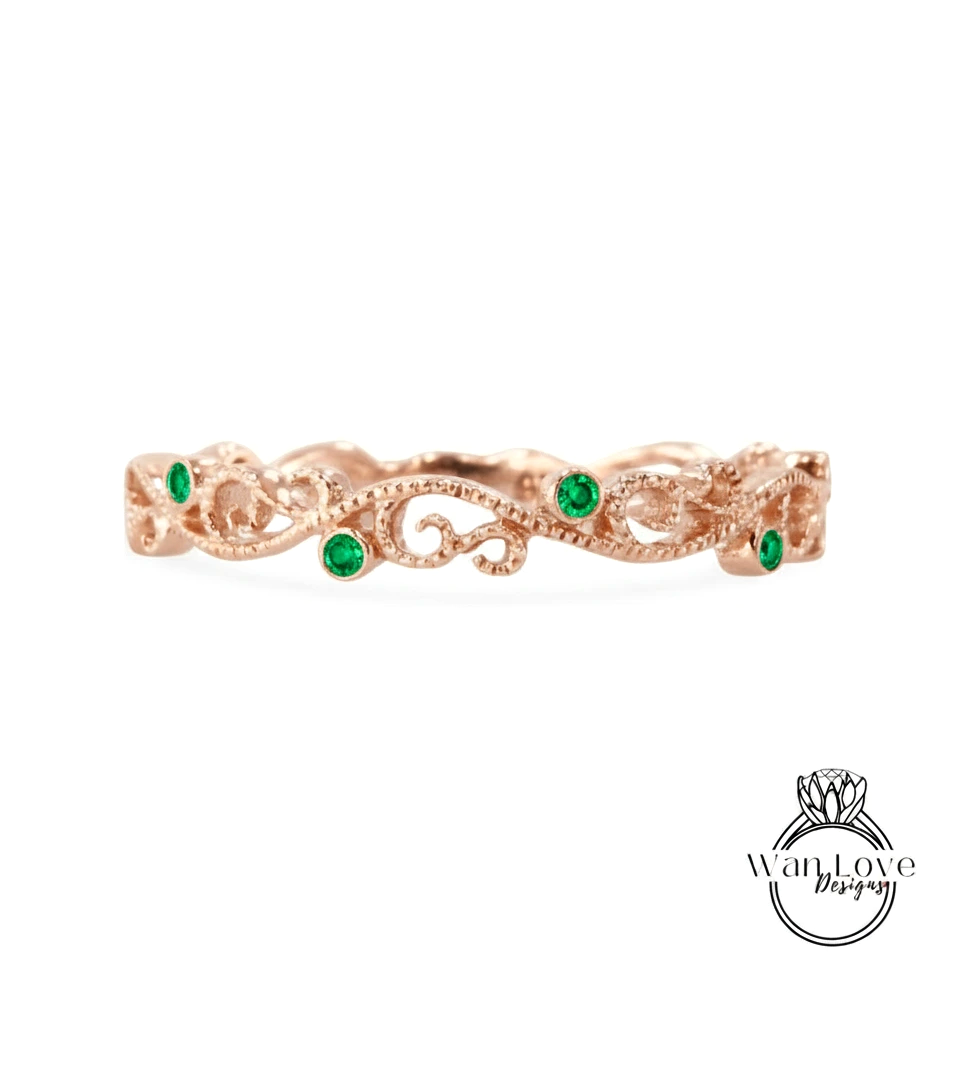 a rose gold ring with a decorative scroll design and green gemstones.