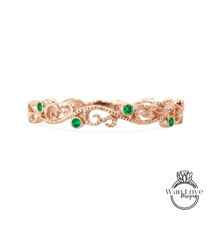 a rose gold ring with a decorative scroll design and green gemstones.