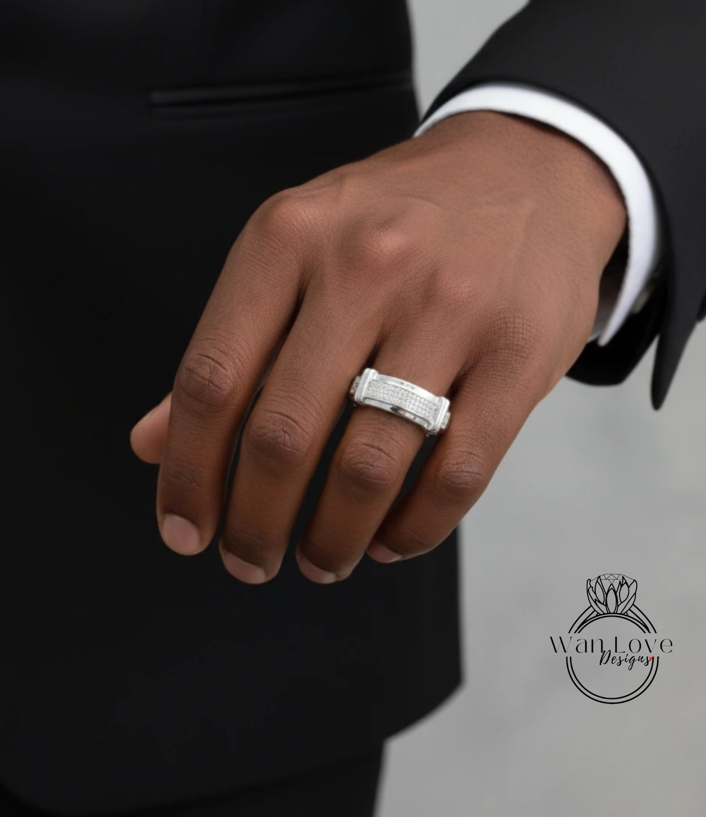A close-up of a person's hand wearing a silver ring, with a black suit jacket visible in the background.