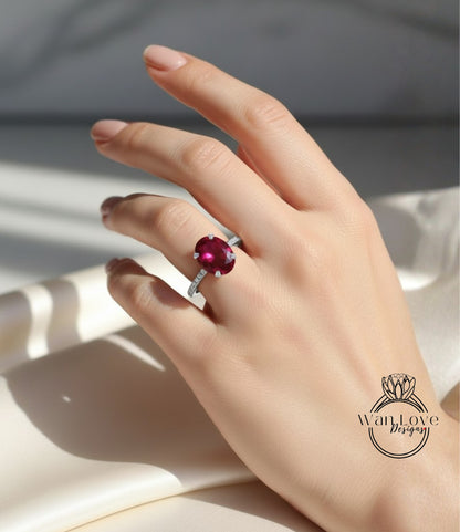 A close-up of a hand wearing a ring with a large, vibrant red gemstone.
