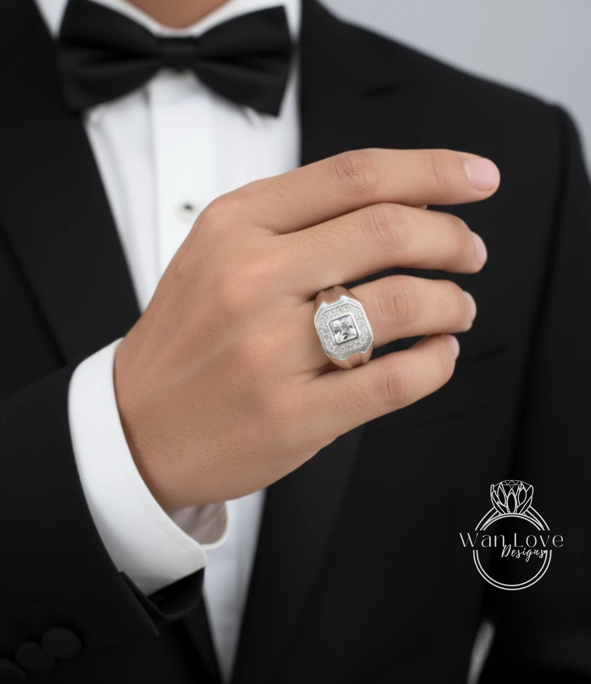 A close-up of a person's hand wearing a diamond ring, with a black tuxedo jacket visible in the background.