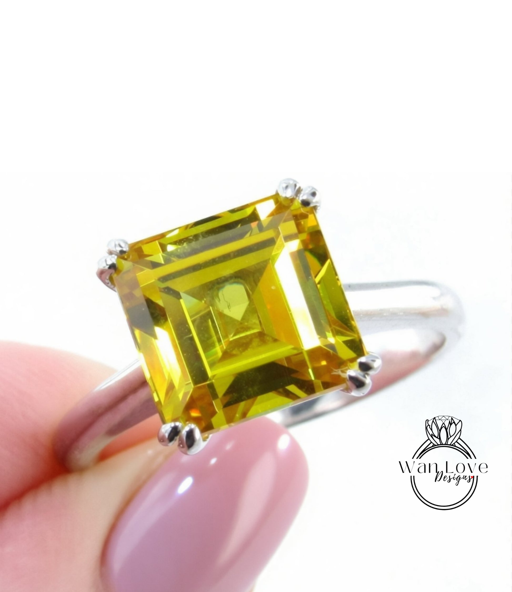 A close-up image of a person's hand holding a ring with a large, square-cut yellow gemstone.