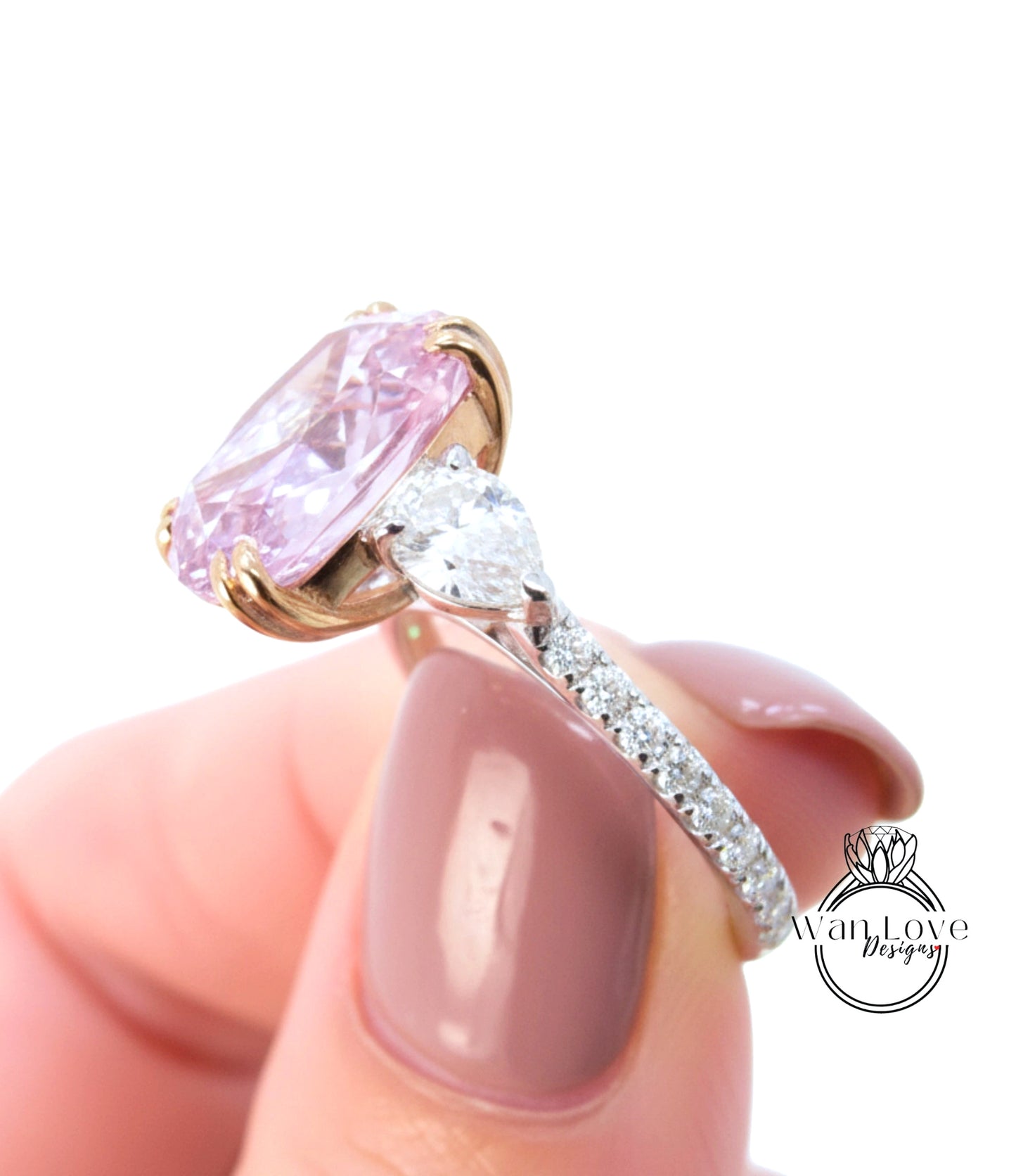 A close-up of a person's hand holding a pink diamond engagement ring with a large central diamond and smaller diamonds around the band.
