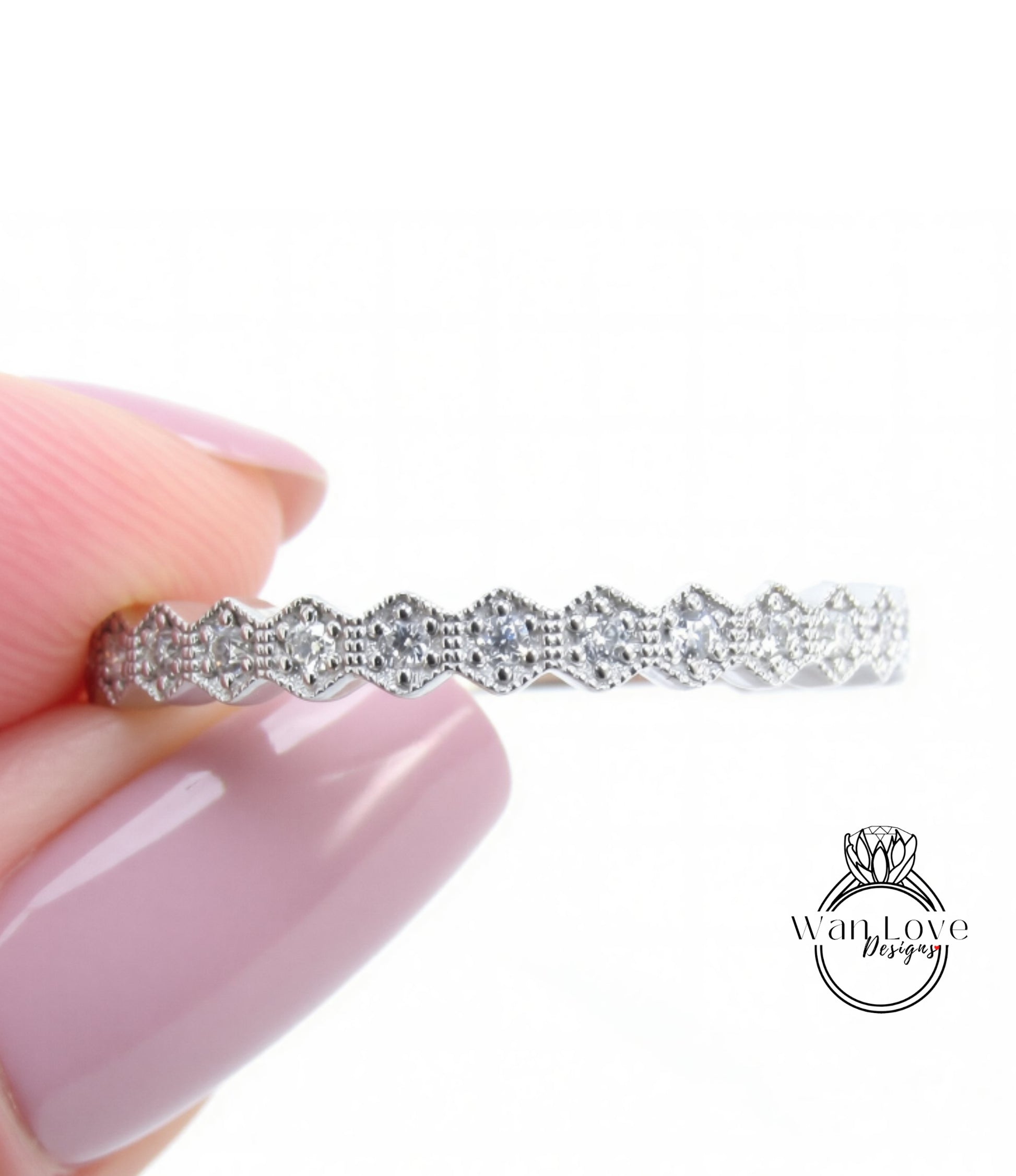 A close-up of a person's hand holding a silver ring with a row of small diamonds along the band.