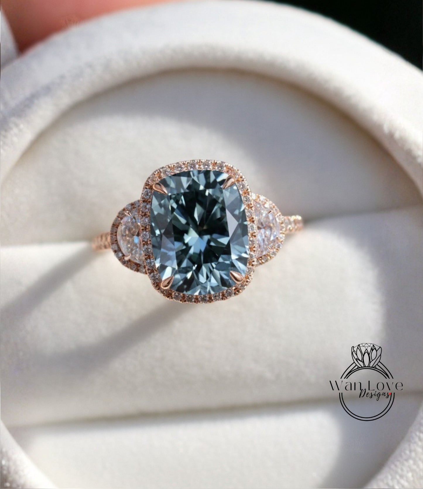 A close-up image of a beautiful engagement ring with a large blue gemstone set in a halo of smaller diamonds, displayed on a white velvet background.