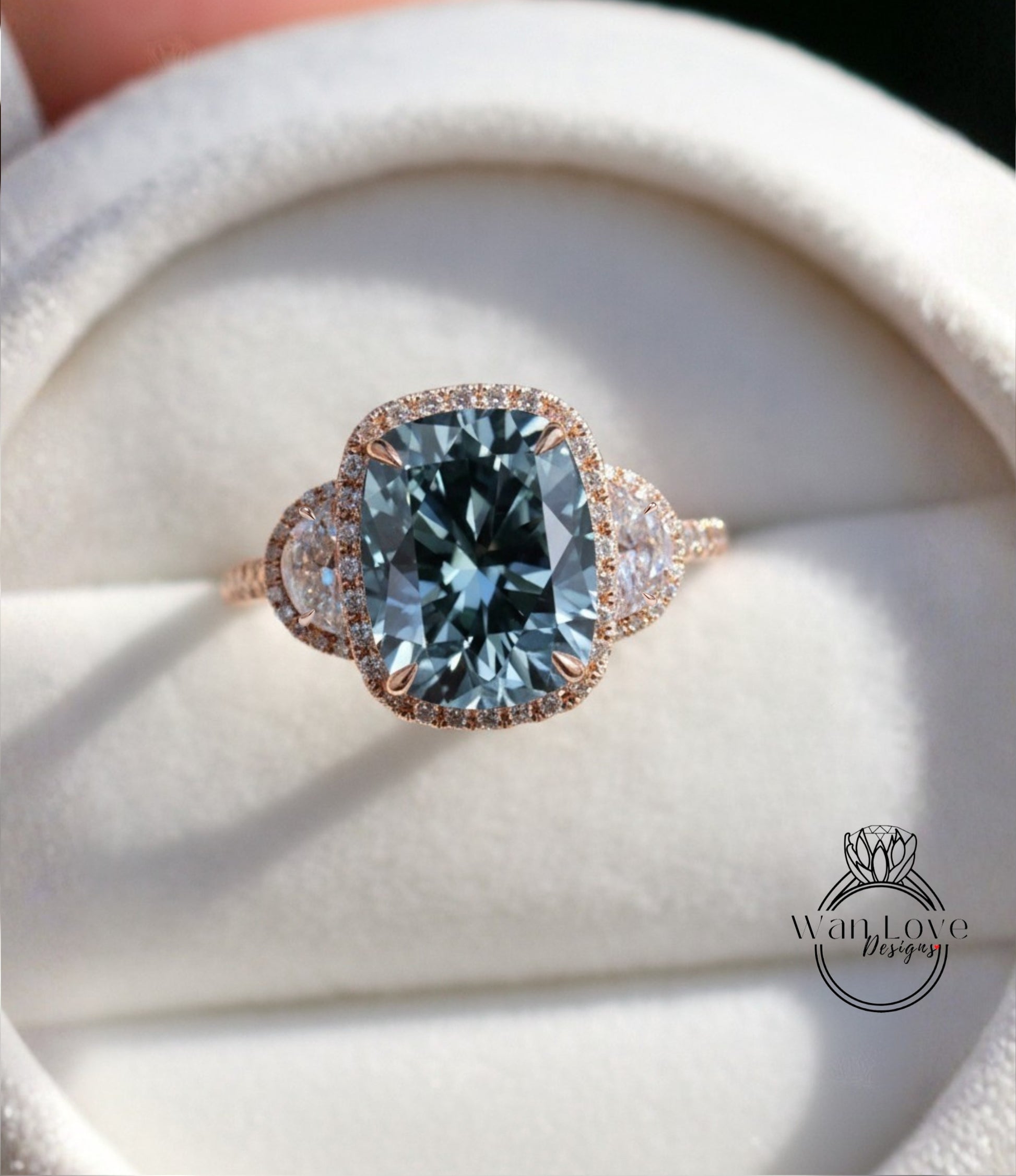 A close-up image of a beautiful engagement ring with a large blue gemstone set in a halo of smaller diamonds, displayed on a white velvet background.