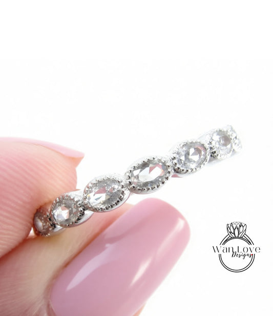 A close-up image of a person's hand holding a silver ring with a row of oval-shaped clear gemstones.