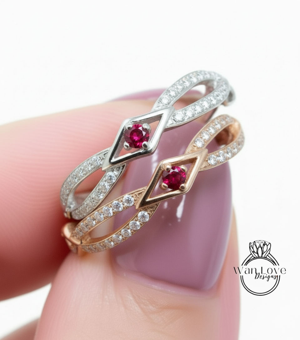 A close-up of a person's hand wearing a ring with two gemstone stones, one red and one silver, set in a silver band with a diamond-encrusted band.
