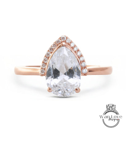 A rose gold ring with a large, clear pear-shaped gemstone set in the center, surrounded by smaller diamonds.