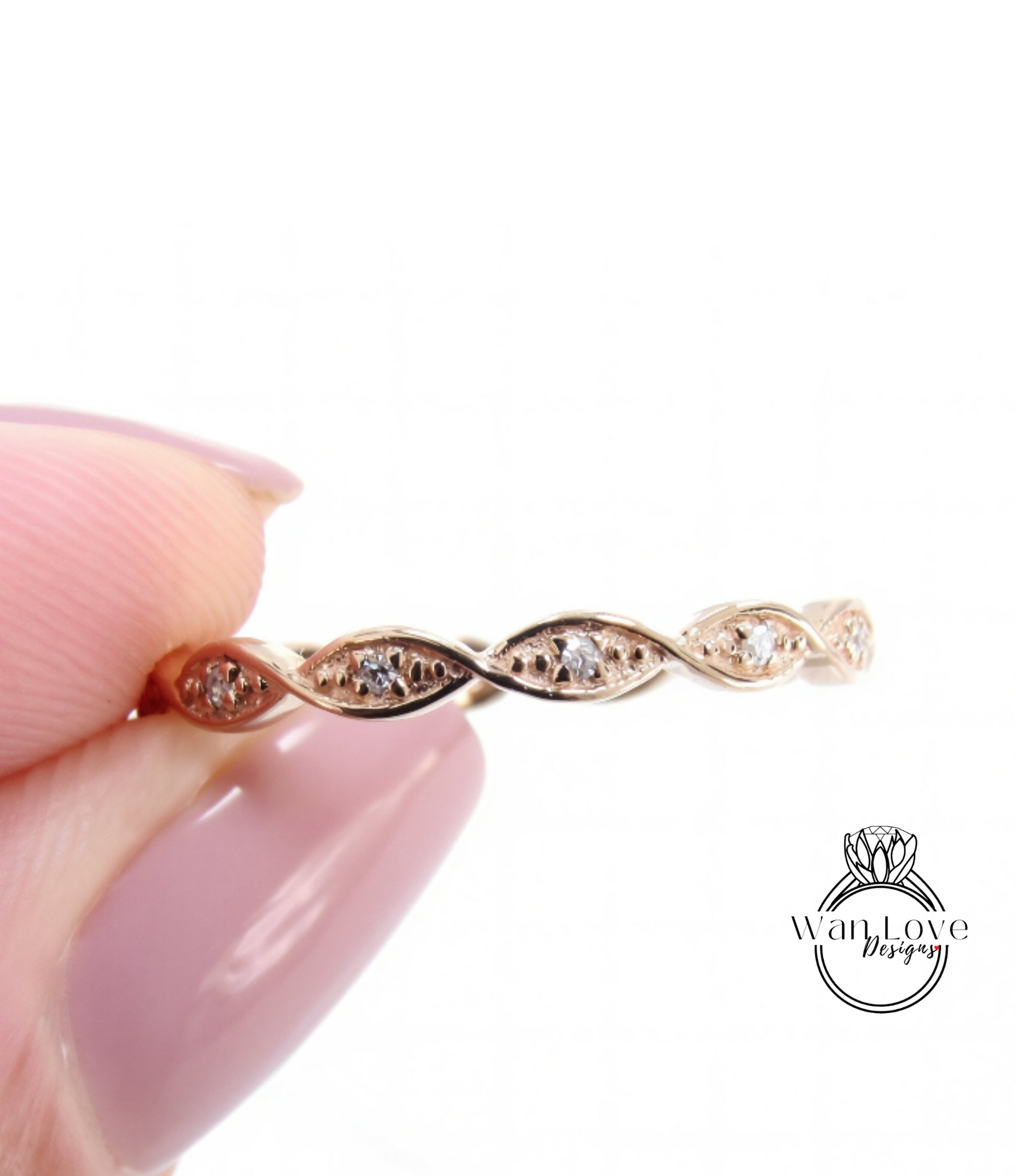 A close-up image of a person's hand holding a delicate gold ring with a twisted design and small diamonds.
