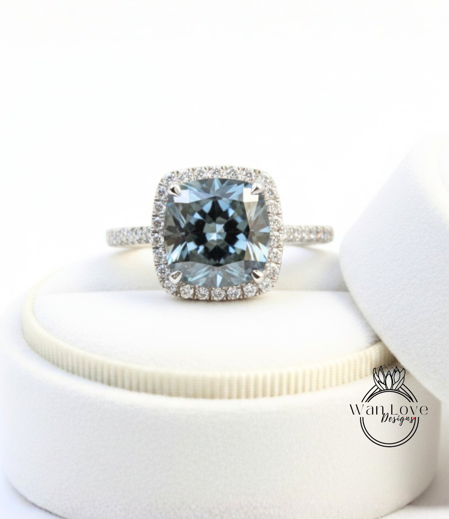 A diamond engagement ring with a large blue gemstone set in a halo of smaller diamonds, displayed on a white stand.