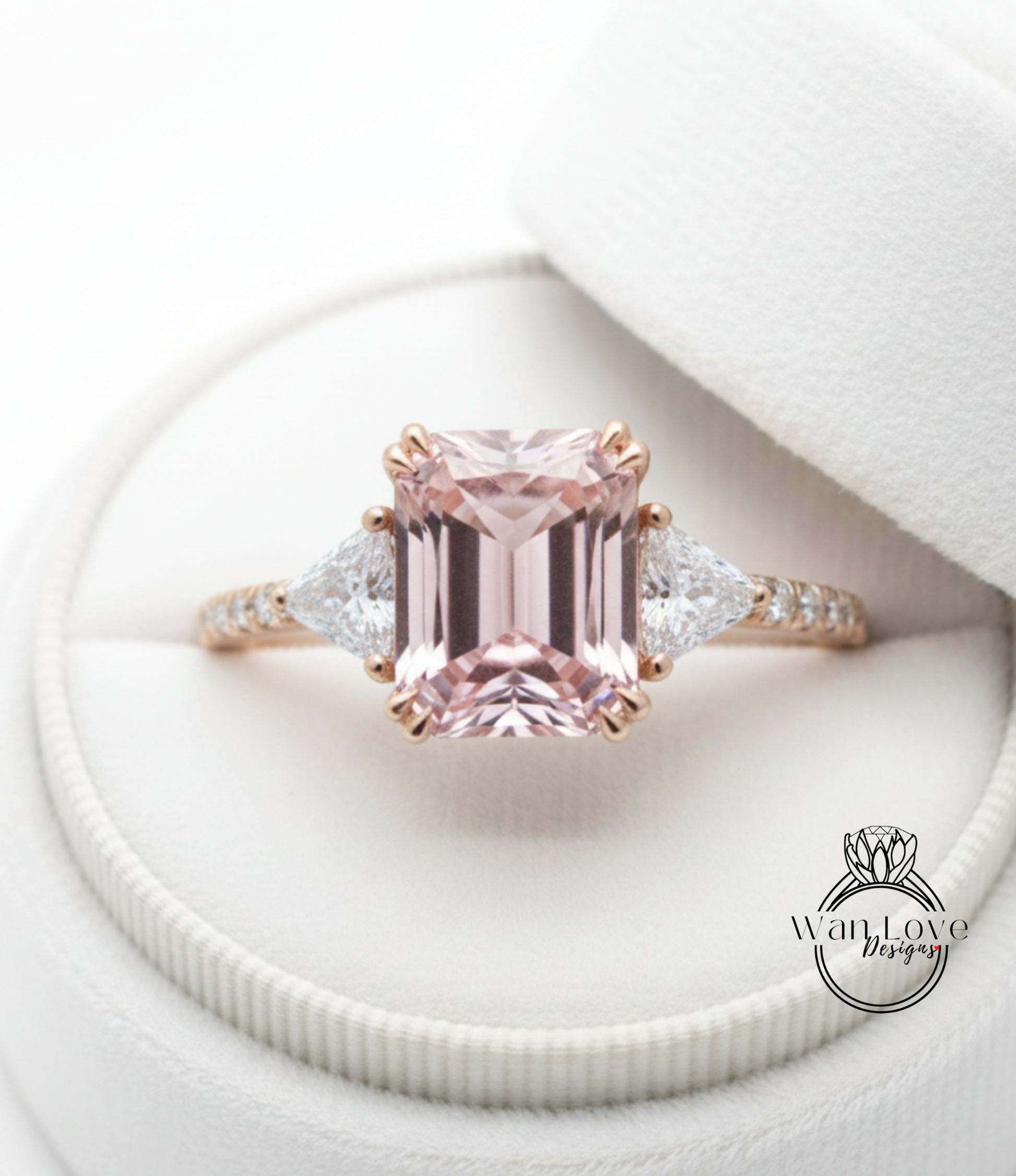 A beautiful pink gemstone engagement ring with a large central gemstone surrounded by smaller triangular gemstones, displayed in a white jewelry box.