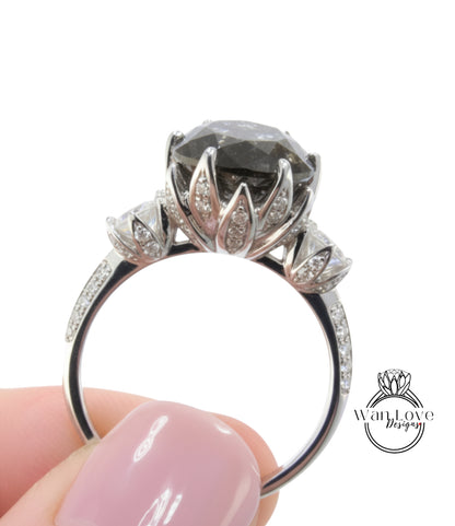 A close-up image of a person's hand holding a silver ring with a large, dark gemstone, likely a diamond, on the ring.