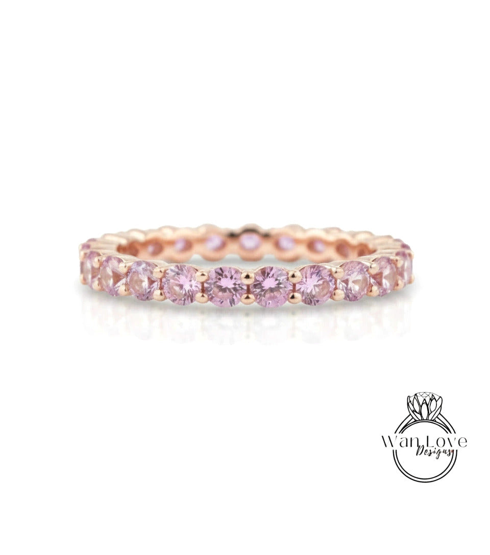 A delicate gold ring with a row of pink gemstones, likely a diamond, set in a delicate band.