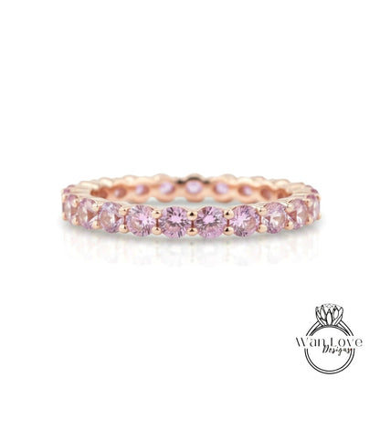 A delicate gold ring with a row of pink gemstones, likely a diamond, set in a delicate band.