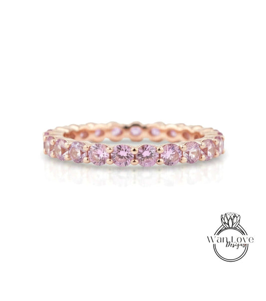 A delicate gold ring with a row of pink gemstones, likely a diamond, set in a delicate band.