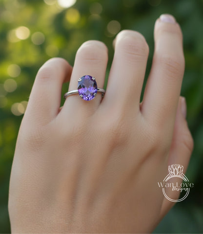 A close-up of a hand wearing a ring with a large purple gemstone, against a blurred green background.