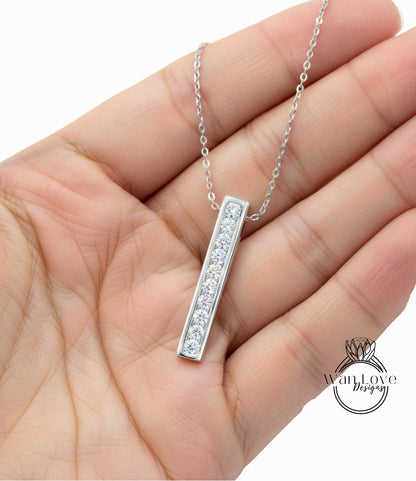 A hand holding a silver necklace with a rectangular pendant featuring a row of small diamonds.