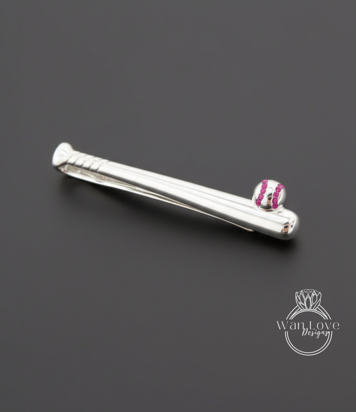 A silver tie clip with a baseball design on it, placed on a dark background.