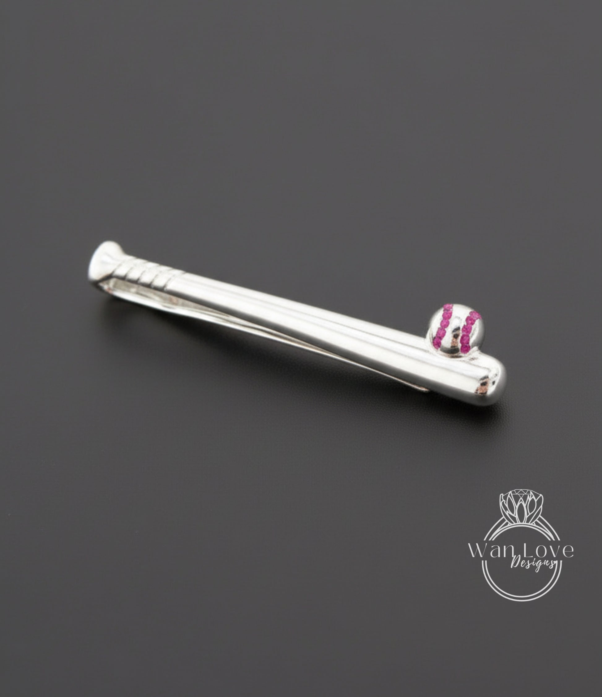 A silver tie clip with a baseball design on it, placed on a dark background.